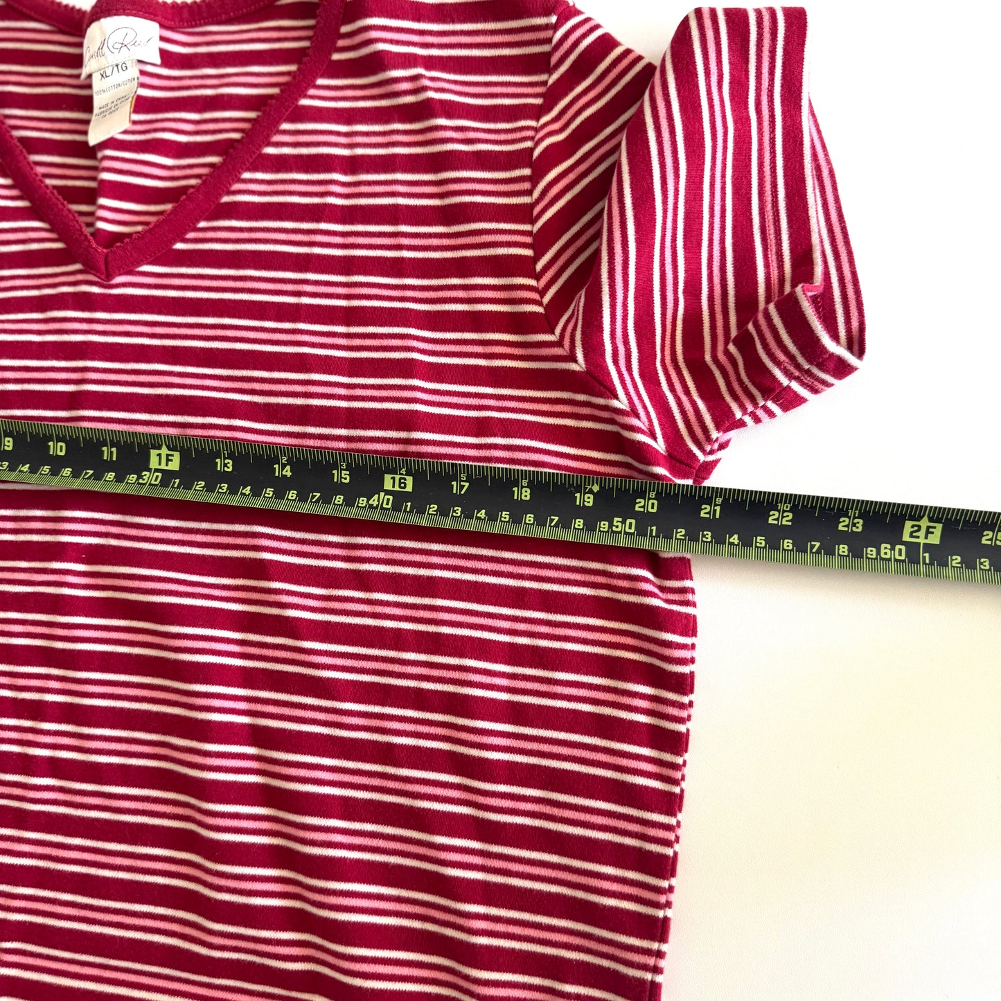 White, pink, and red striped t-shirt with a v-neck collar on a white backdrop - plus a measuring tape laid out on it.