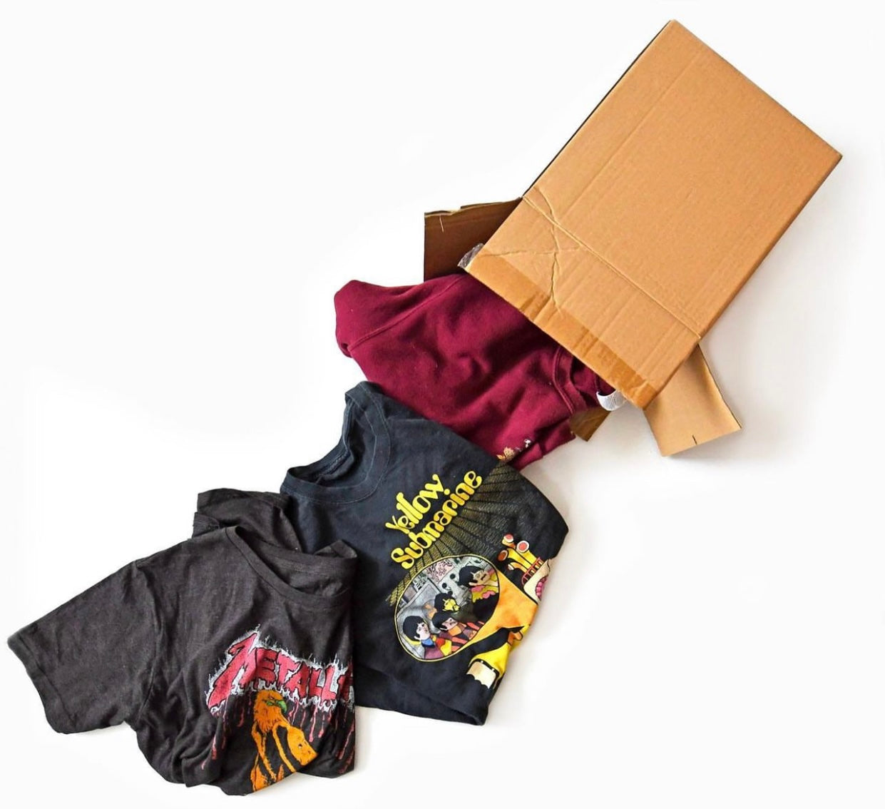 Shipping box with random t-shirts falling out of it with a white background. 